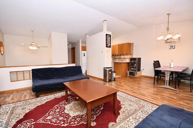 living room with ceiling fan with notable chandelier, light wood-type flooring, and vaulted ceiling