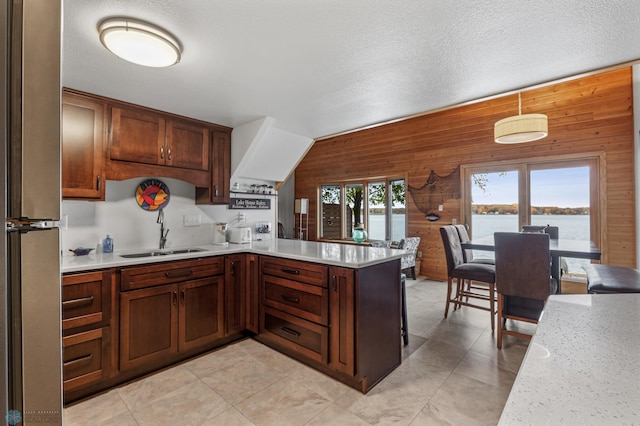 kitchen featuring wood walls, a water view, decorative light fixtures, sink, and a textured ceiling