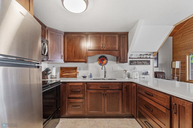 kitchen featuring wood walls, light tile patterned flooring, sink, kitchen peninsula, and appliances with stainless steel finishes