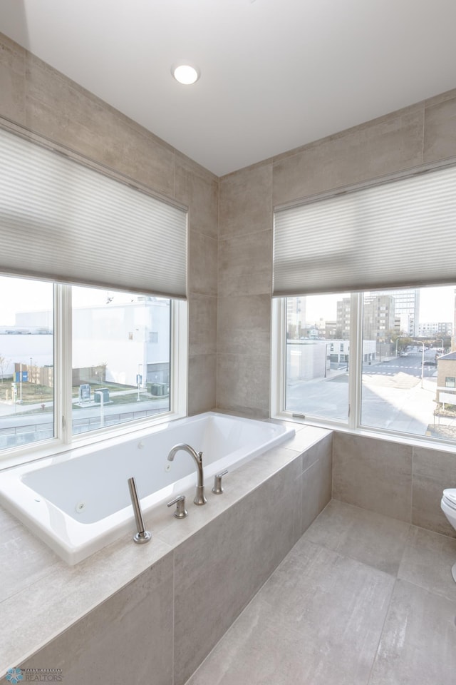 bathroom with toilet, tiled tub, and plenty of natural light