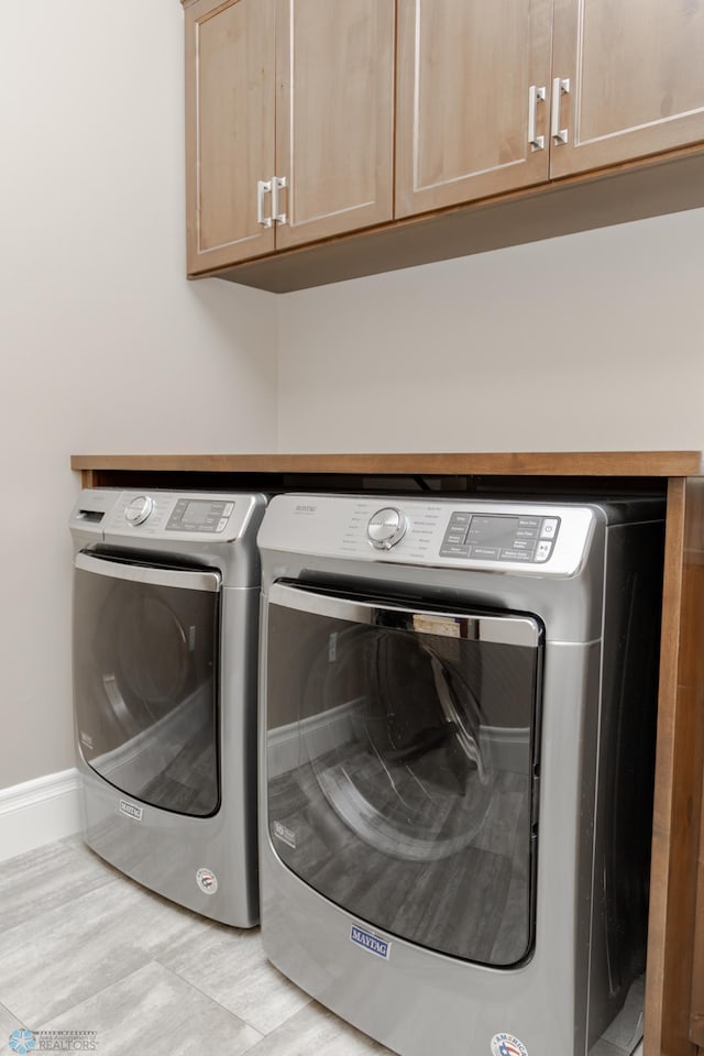 laundry room featuring washer and clothes dryer, light hardwood / wood-style floors, and cabinets