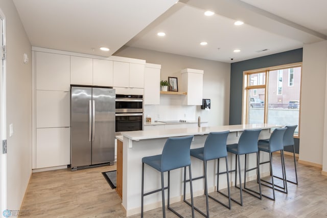 kitchen with appliances with stainless steel finishes, light wood-type flooring, white cabinetry, and an island with sink