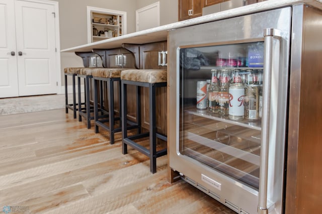 bar with light hardwood / wood-style flooring and stainless steel fridge