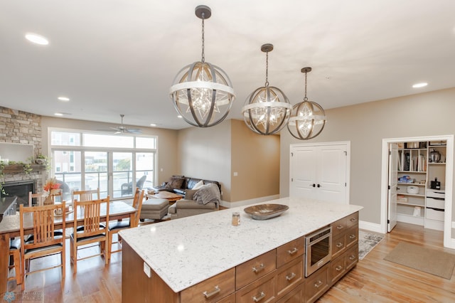 kitchen with a kitchen island, stainless steel microwave, ceiling fan with notable chandelier, pendant lighting, and light hardwood / wood-style floors