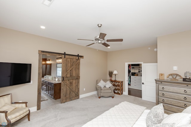 bedroom with a closet, a walk in closet, a barn door, light colored carpet, and ceiling fan