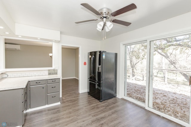 kitchen with a wall unit AC, dark hardwood / wood-style flooring, ceiling fan, black fridge, and gray cabinets