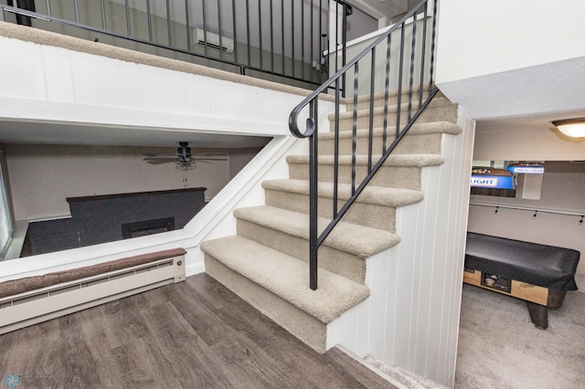 stairway with a baseboard heating unit and wood-type flooring