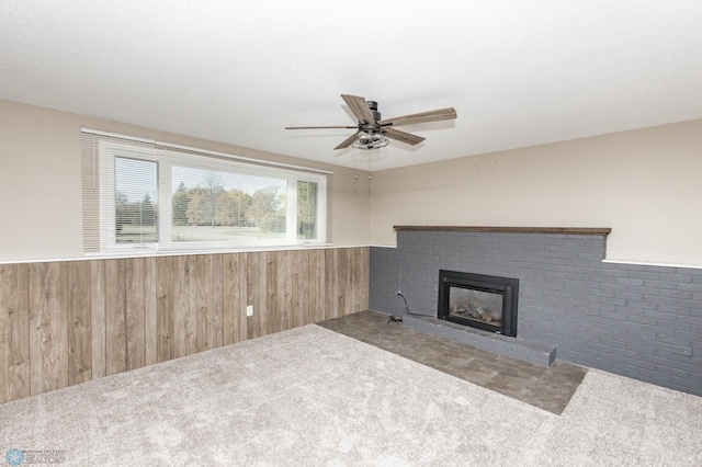 unfurnished living room featuring ceiling fan, carpet floors, wooden walls, and a fireplace