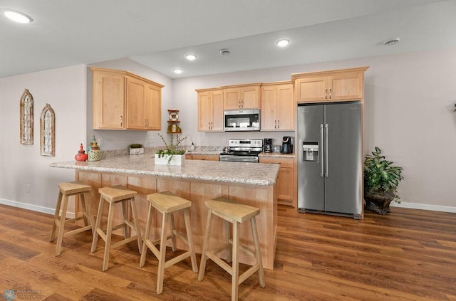 kitchen with light hardwood / wood-style floors, appliances with stainless steel finishes, light brown cabinetry, and kitchen peninsula