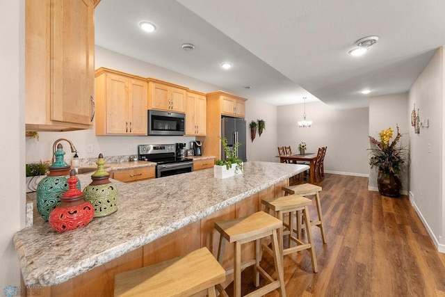 kitchen with light brown cabinets, kitchen peninsula, light stone countertops, appliances with stainless steel finishes, and dark hardwood / wood-style flooring