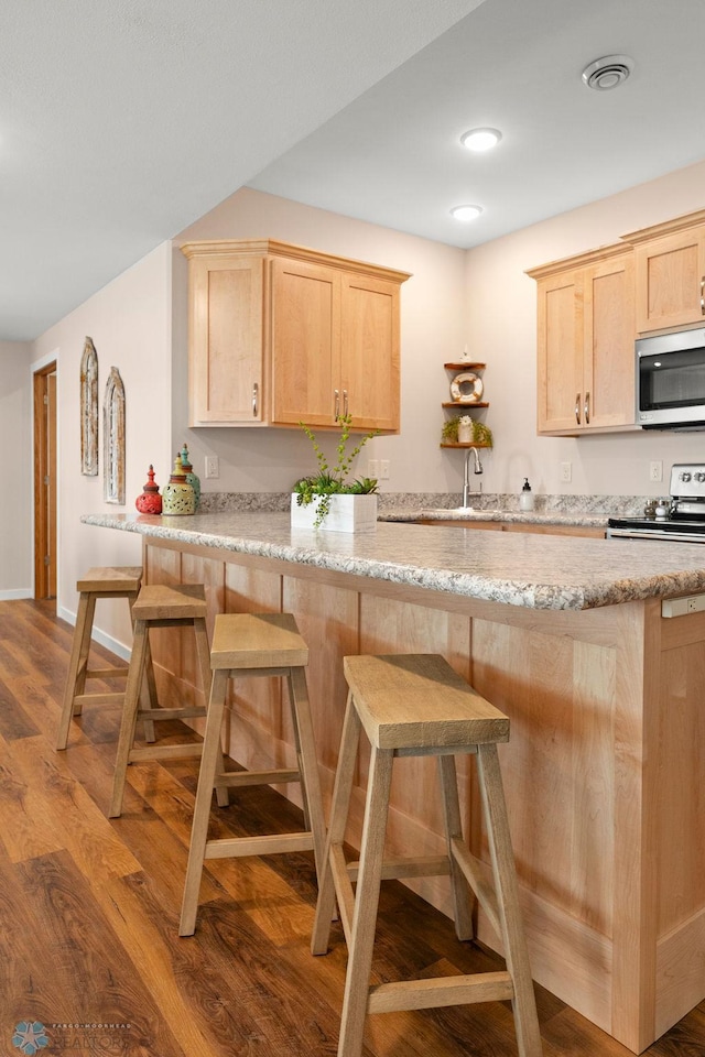 kitchen featuring light brown cabinets, kitchen peninsula, wood-type flooring, light stone countertops, and range