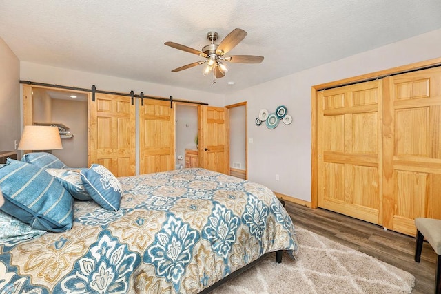 bedroom featuring a closet, wood-type flooring, a barn door, a textured ceiling, and ceiling fan