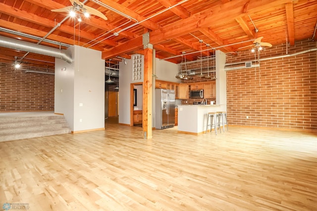 unfurnished living room featuring brick wall, light hardwood / wood-style flooring, a towering ceiling, and ceiling fan