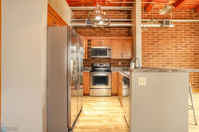 kitchen with sink, a kitchen bar, stainless steel appliances, brick wall, and light hardwood / wood-style flooring