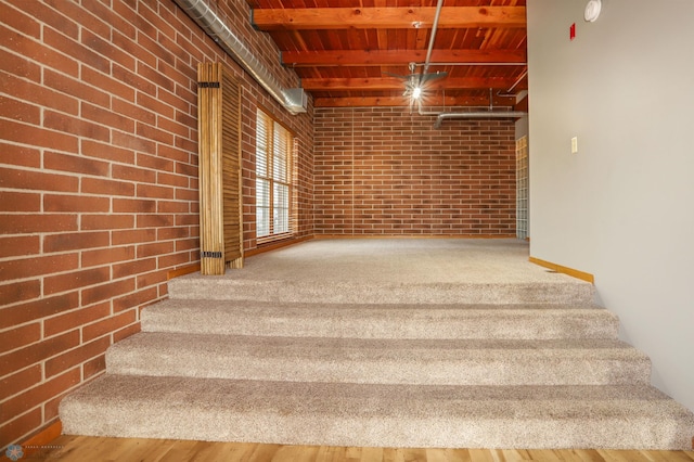 staircase featuring brick wall, beamed ceiling, and hardwood / wood-style floors