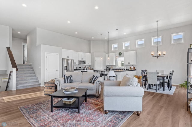 living room with light hardwood / wood-style floors, a notable chandelier, sink, and a towering ceiling