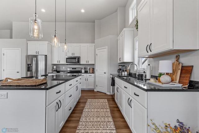 kitchen with appliances with stainless steel finishes, sink, hanging light fixtures, white cabinets, and dark wood-type flooring