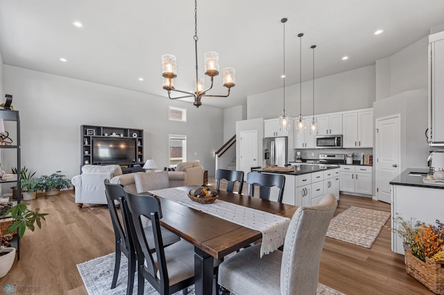 dining room with sink, light hardwood / wood-style flooring, a notable chandelier, and a towering ceiling