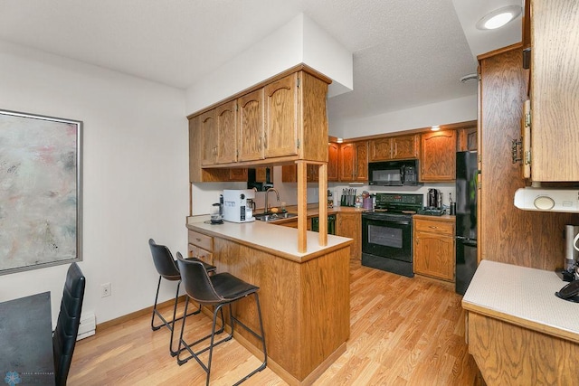 kitchen with kitchen peninsula, a breakfast bar area, black appliances, light hardwood / wood-style floors, and sink