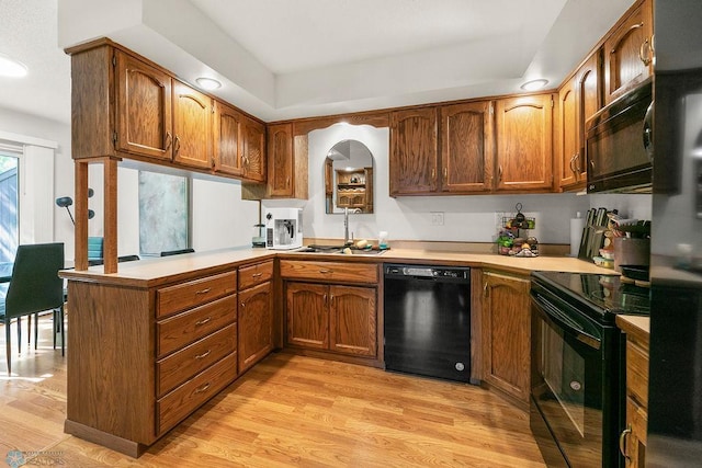 kitchen with sink, black appliances, light hardwood / wood-style flooring, and kitchen peninsula