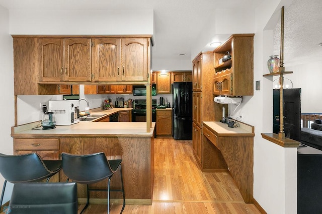 kitchen featuring a breakfast bar area, kitchen peninsula, sink, black appliances, and light hardwood / wood-style floors