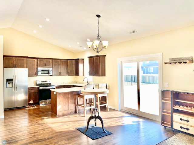 kitchen featuring light hardwood / wood-style floors, stainless steel appliances, lofted ceiling, decorative light fixtures, and a breakfast bar area