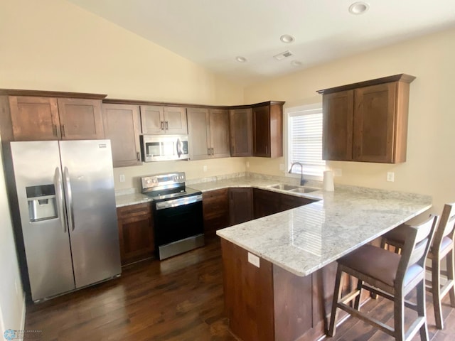 kitchen featuring dark wood-type flooring, stainless steel appliances, sink, vaulted ceiling, and light stone counters