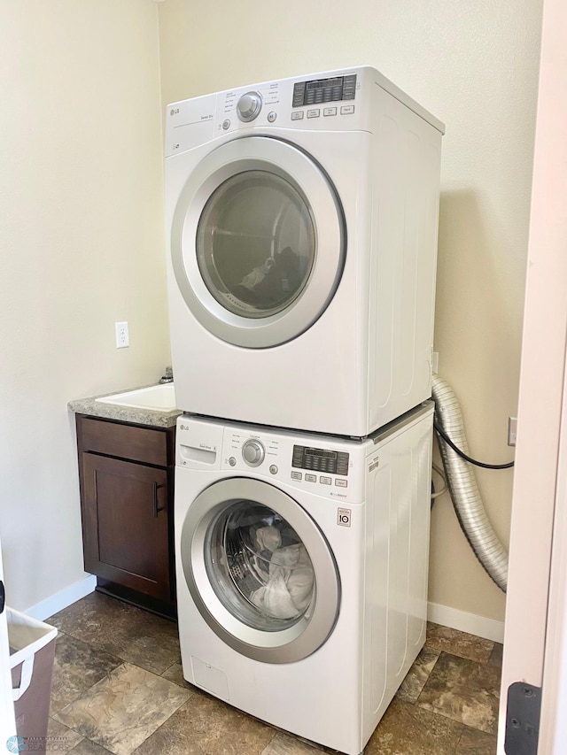 washroom featuring sink, stacked washing maching and dryer, and cabinets