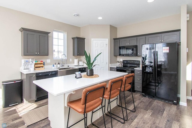 kitchen featuring a breakfast bar area, a kitchen island, dark hardwood / wood-style flooring, black appliances, and sink