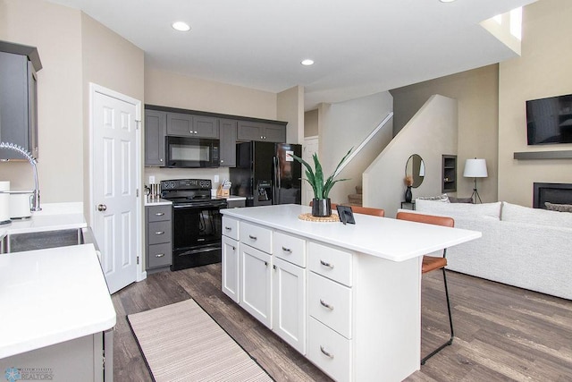 kitchen with a kitchen island, dark hardwood / wood-style floors, a breakfast bar area, gray cabinetry, and black appliances