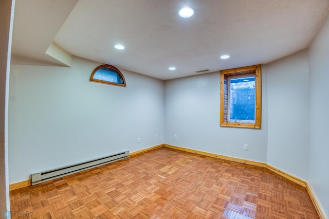 spare room featuring a baseboard heating unit, a textured ceiling, and light parquet flooring