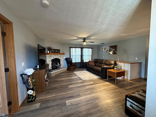 living room with dark wood-type flooring, ceiling fan, a textured ceiling, and a fireplace