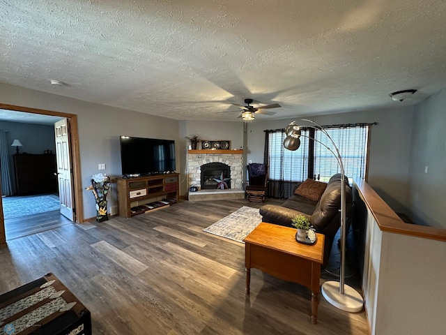 living room with a stone fireplace, hardwood / wood-style floors, a textured ceiling, and ceiling fan