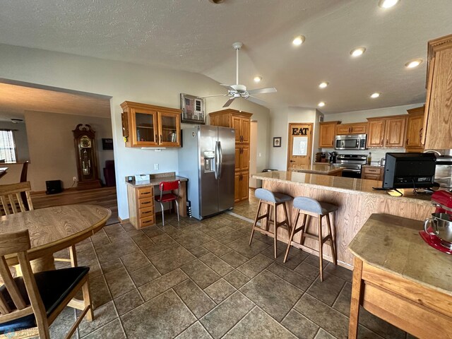 kitchen featuring kitchen peninsula, stainless steel appliances, a breakfast bar, vaulted ceiling, and ceiling fan