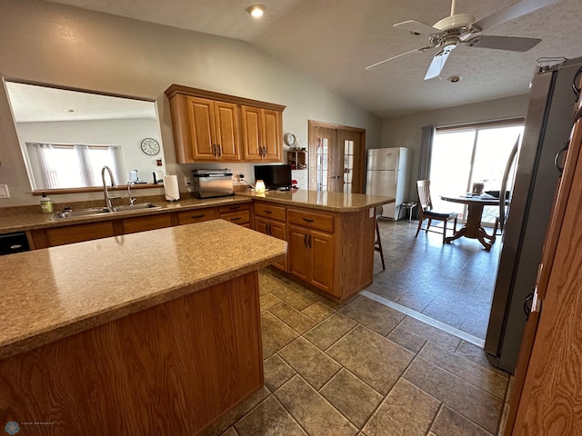 kitchen with sink, kitchen peninsula, stainless steel fridge, vaulted ceiling, and a breakfast bar area