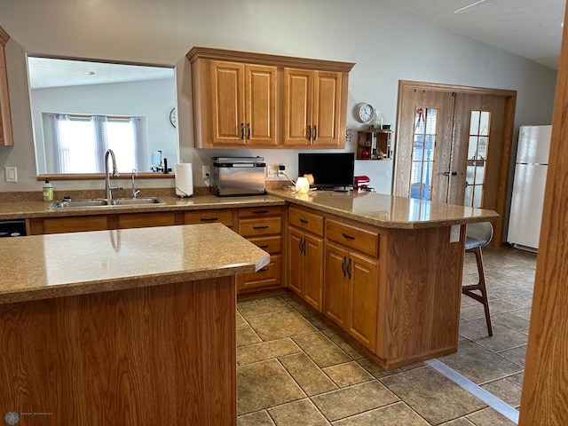 kitchen featuring sink, vaulted ceiling, kitchen peninsula, and white refrigerator