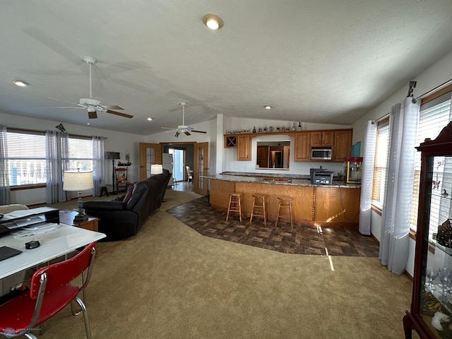 kitchen featuring kitchen peninsula, stainless steel microwave, a textured ceiling, vaulted ceiling, and dark colored carpet