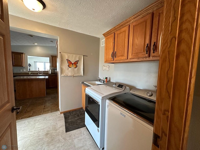 washroom with cabinets, a textured ceiling, sink, and washer and clothes dryer