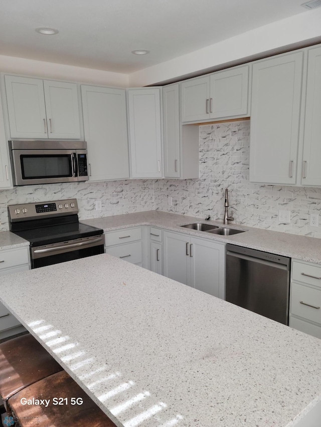 kitchen featuring appliances with stainless steel finishes, sink, white cabinets, light stone counters, and decorative backsplash