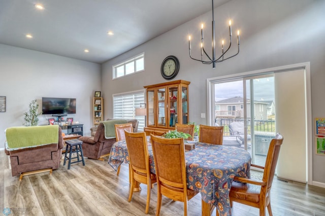 dining room with a towering ceiling, a notable chandelier, a healthy amount of sunlight, and light wood-type flooring