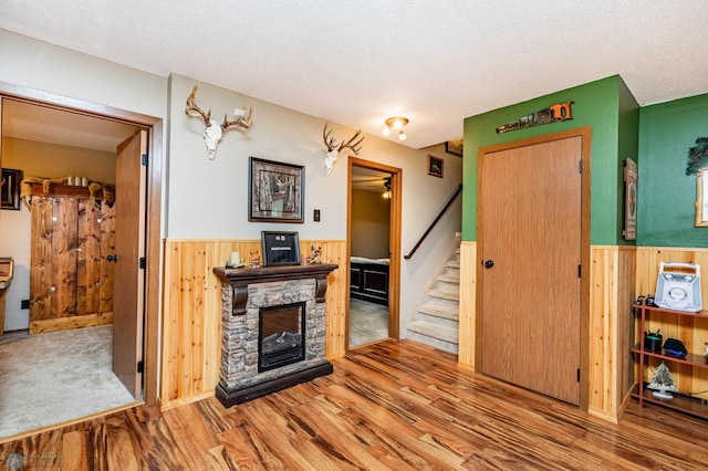 interior space featuring hardwood / wood-style floors, a stone fireplace, a textured ceiling, and wood walls