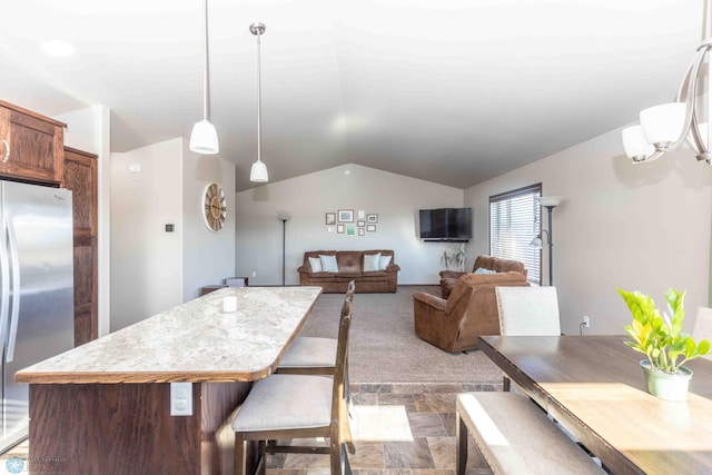 kitchen featuring lofted ceiling, stainless steel fridge, hanging light fixtures, light colored carpet, and a center island