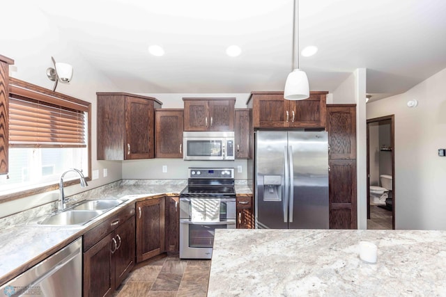 kitchen featuring pendant lighting, sink, light stone countertops, and stainless steel appliances