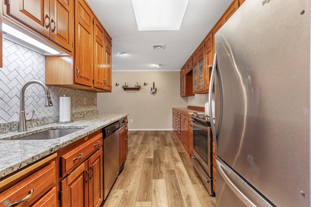 kitchen with decorative backsplash, appliances with stainless steel finishes, sink, light hardwood / wood-style floors, and light stone counters