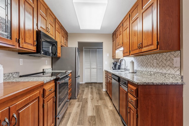 kitchen featuring backsplash, appliances with stainless steel finishes, light wood-type flooring, sink, and light stone counters