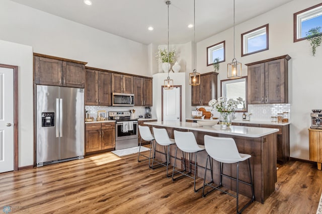 kitchen with a kitchen island, stainless steel appliances, hardwood / wood-style floors, pendant lighting, and tasteful backsplash