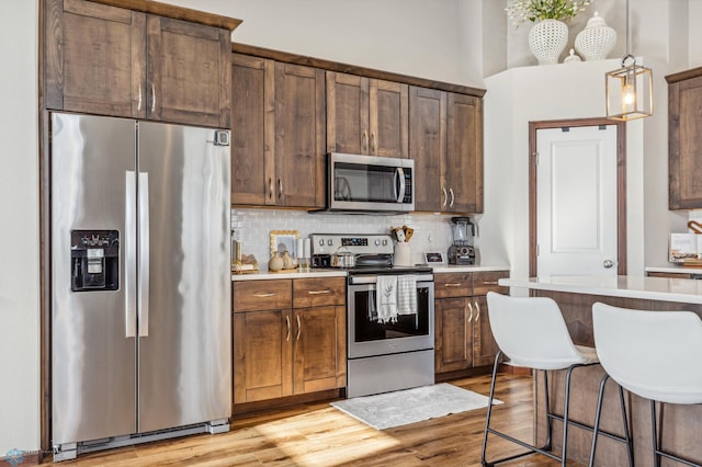 kitchen featuring tasteful backsplash, appliances with stainless steel finishes, a kitchen breakfast bar, light wood-type flooring, and pendant lighting