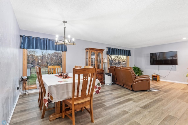 dining area with light hardwood / wood-style floors, a notable chandelier, and a textured ceiling