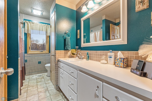 bathroom featuring vanity, toilet, tile walls, and a textured ceiling