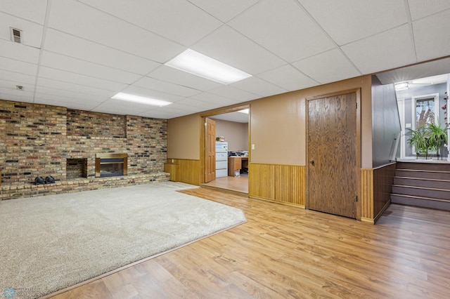 interior space featuring light hardwood / wood-style floors, a brick fireplace, a paneled ceiling, and wooden walls